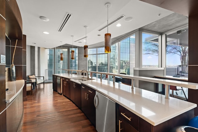 kitchen with hanging light fixtures, dark wood-type flooring, floor to ceiling windows, and an island with sink