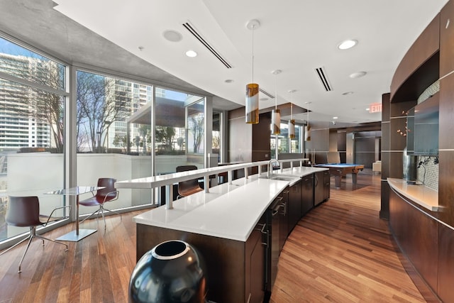 kitchen with an island with sink, decorative light fixtures, pool table, light wood-type flooring, and sink