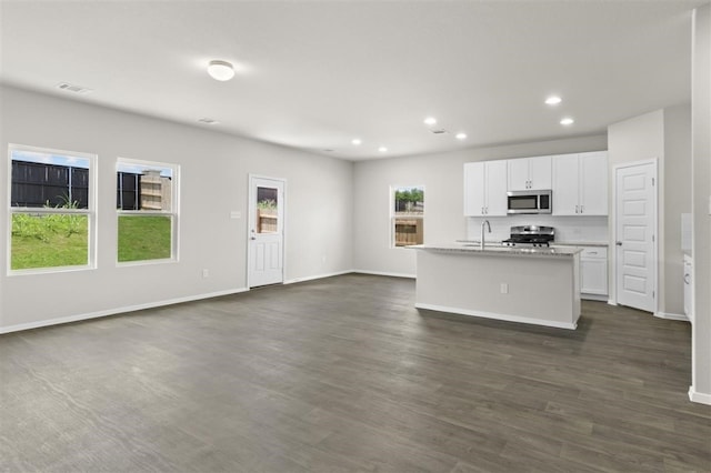 kitchen with a kitchen island with sink, stainless steel appliances, dark hardwood / wood-style flooring, light stone counters, and white cabinets