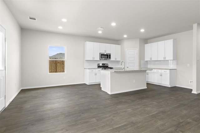 kitchen featuring an island with sink, tasteful backsplash, dark hardwood / wood-style flooring, white cabinets, and appliances with stainless steel finishes