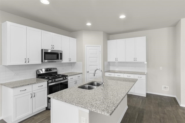 kitchen with light stone countertops, an island with sink, white cabinetry, appliances with stainless steel finishes, and sink