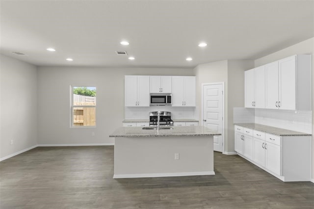 kitchen featuring stainless steel appliances, a center island with sink, light stone countertops, and white cabinetry