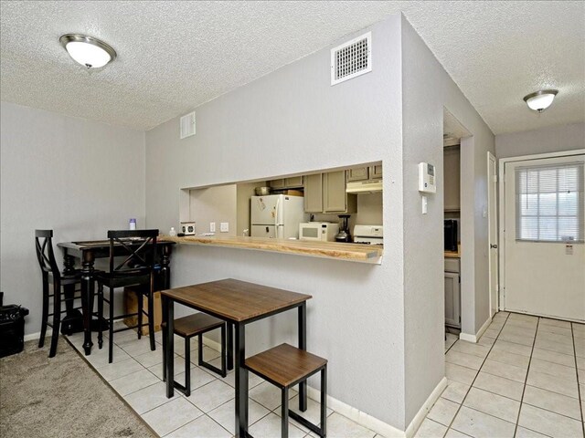 7825 Beauregard Cir Unit 5, Austin, TX 78745 - kitchen with white appliances, a textured ceiling, light tile patterned flooring, a kitchen bar, and a peninsula