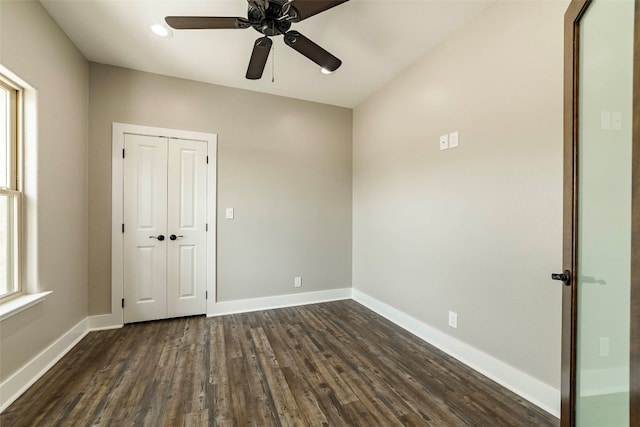 unfurnished bedroom featuring multiple windows, dark wood-type flooring, ceiling fan, and a closet