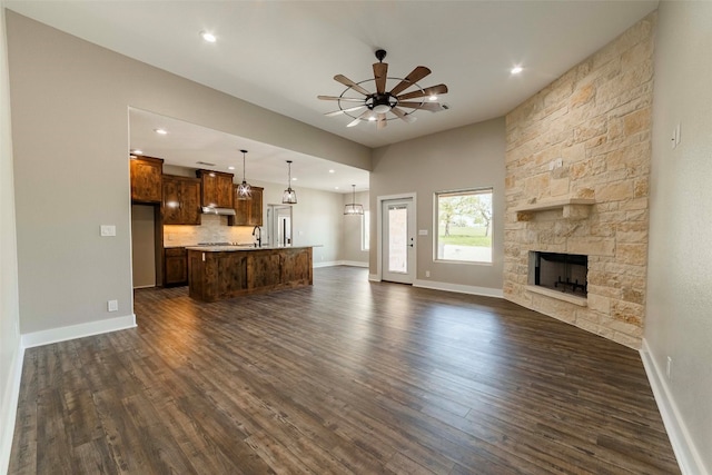 unfurnished living room with ceiling fan, sink, a fireplace, and dark wood-type flooring