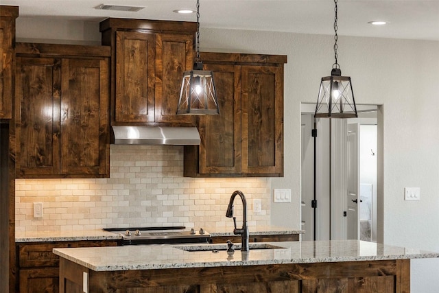 kitchen featuring decorative backsplash, light stone counters, exhaust hood, and sink