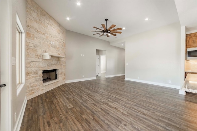 unfurnished living room with a stone fireplace, dark hardwood / wood-style floors, and ceiling fan