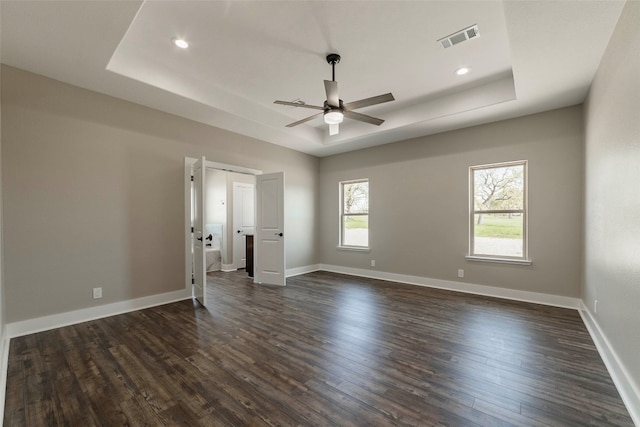 empty room with ceiling fan, a tray ceiling, and dark hardwood / wood-style floors