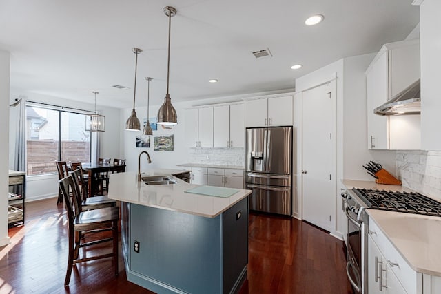 kitchen featuring a kitchen island with sink, stainless steel appliances, hanging light fixtures, and white cabinetry