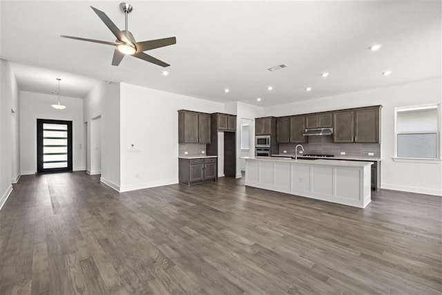 kitchen with a kitchen island with sink, backsplash, sink, appliances with stainless steel finishes, and dark hardwood / wood-style flooring