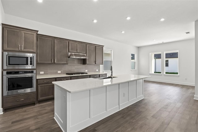 kitchen featuring decorative backsplash, dark hardwood / wood-style flooring, stainless steel appliances, a kitchen island with sink, and sink