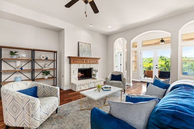 living room with french doors, hardwood / wood-style floors, ceiling fan, and a stone fireplace