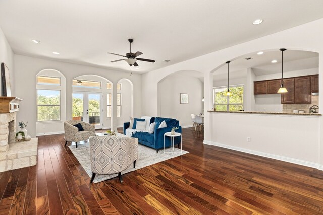 living room with plenty of natural light, ceiling fan, dark hardwood / wood-style floors, and a stone fireplace