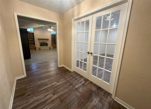 hallway featuring brick wall, a textured ceiling, dark wood-type flooring, and french doors