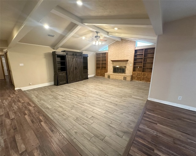 unfurnished living room featuring dark hardwood / wood-style flooring, a barn door, ceiling fan, brick wall, and a fireplace