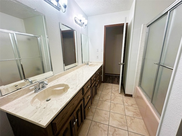 bathroom featuring tile flooring, shower / bath combination with glass door, a textured ceiling, dual sinks, and oversized vanity