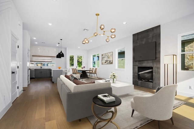 living room with light wood-type flooring, sink, a tile fireplace, and a chandelier