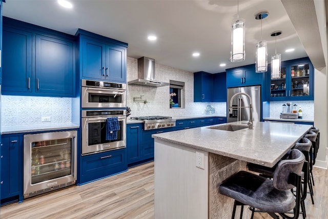 kitchen featuring wall chimney range hood, blue cabinetry, backsplash, and beverage cooler