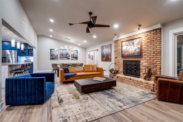 living room with ceiling fan, a brick fireplace, light hardwood / wood-style floors, and vaulted ceiling