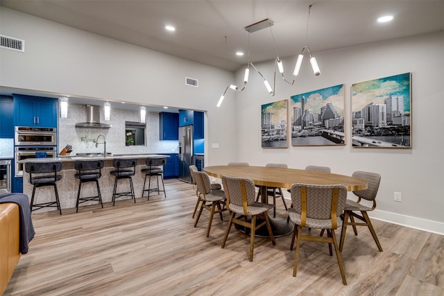 dining area featuring high vaulted ceiling, a notable chandelier, sink, and light wood-type flooring