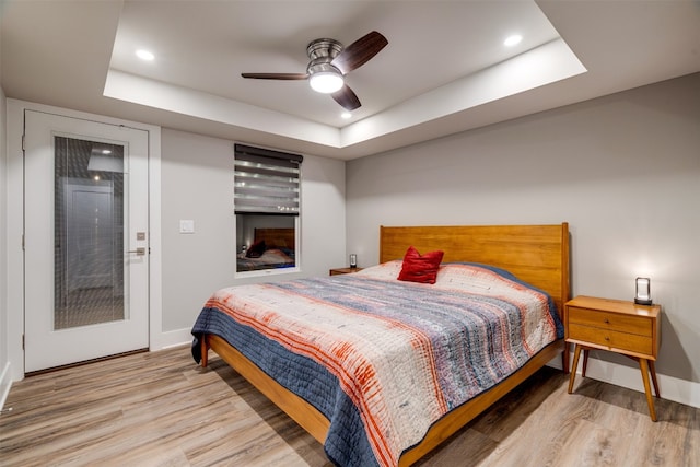 bedroom with a raised ceiling, light hardwood / wood-style floors, and ceiling fan