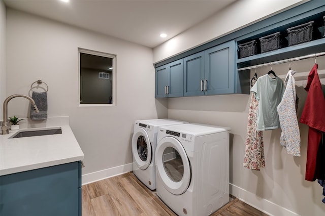 clothes washing area with cabinets, light hardwood / wood-style floors, washing machine and clothes dryer, and sink