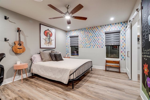 bedroom with a barn door, ceiling fan, and light hardwood / wood-style flooring