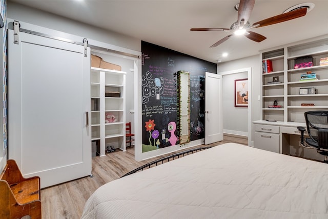 bedroom featuring a barn door, light hardwood / wood-style flooring, and ceiling fan