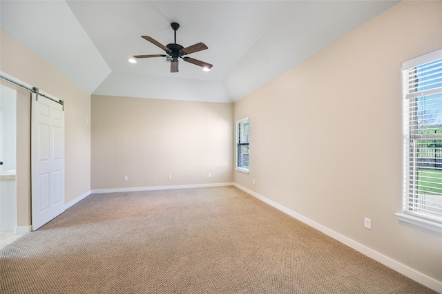 unfurnished bedroom featuring ceiling fan, light carpet, vaulted ceiling, and a barn door