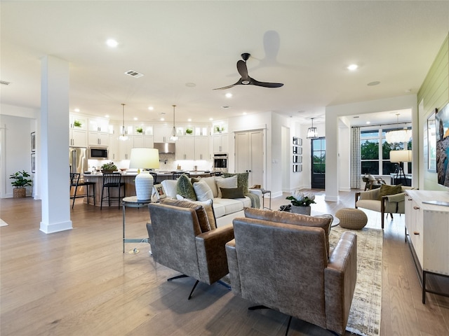 living room featuring decorative columns, light hardwood / wood-style flooring, and ceiling fan with notable chandelier