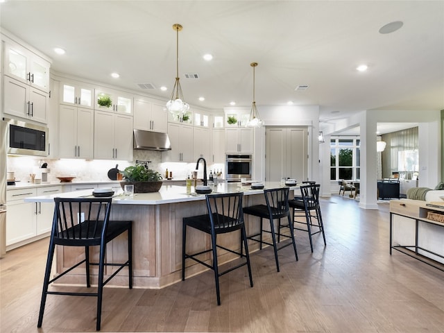 kitchen with appliances with stainless steel finishes, a breakfast bar area, hardwood / wood-style floors, and a kitchen island with sink