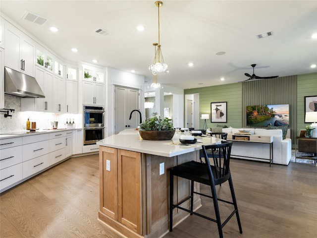 kitchen with a center island with sink, light hardwood / wood-style flooring, ceiling fan with notable chandelier, and white cabinetry