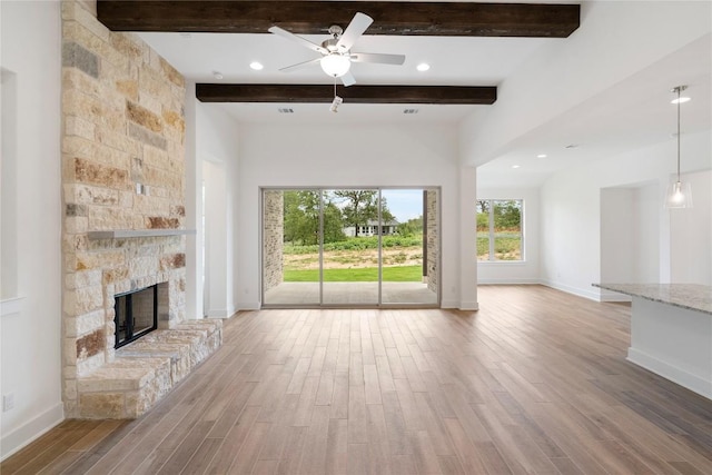 unfurnished living room featuring a ceiling fan, a stone fireplace, wood finished floors, beamed ceiling, and baseboards