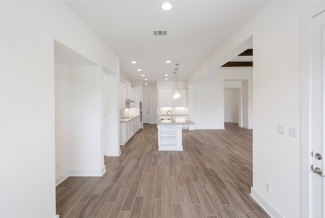 kitchen featuring light hardwood / wood-style flooring, hanging light fixtures, a kitchen island, beam ceiling, and white cabinetry