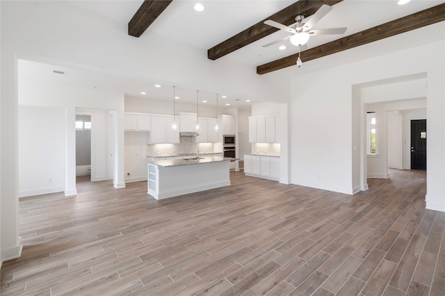 kitchen with an island with sink, sink, light hardwood / wood-style floors, beam ceiling, and white cabinetry