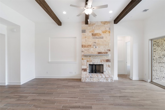 unfurnished living room with beamed ceiling, a stone fireplace, ceiling fan, and hardwood / wood-style floors