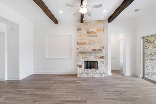 unfurnished living room featuring a stone fireplace, beam ceiling, wood finished floors, and visible vents