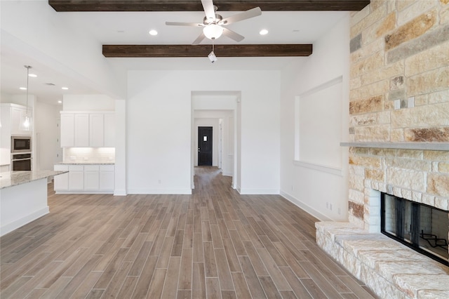 unfurnished living room with a stone fireplace, ceiling fan, light hardwood / wood-style floors, and beam ceiling