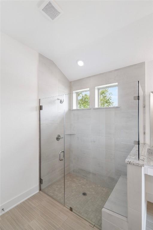 full bath featuring lofted ceiling, a shower stall, visible vents, and baseboards