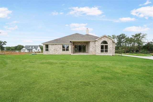 back of property with brick siding, roof with shingles, a chimney, and a yard