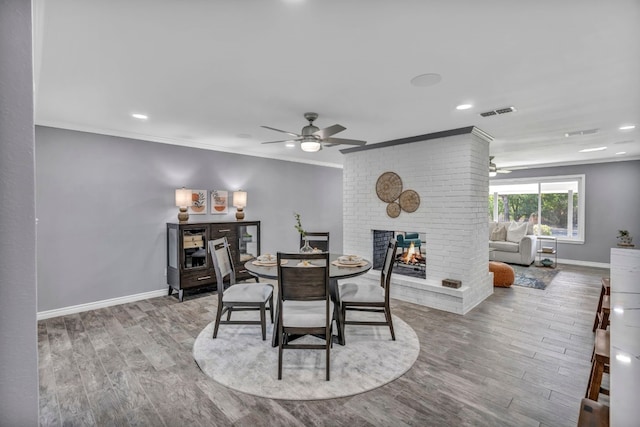 dining space featuring a brick fireplace, ceiling fan, light wood-type flooring, and crown molding