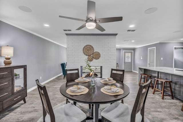 dining room with a fireplace, brick wall, ceiling fan, and light hardwood / wood-style flooring