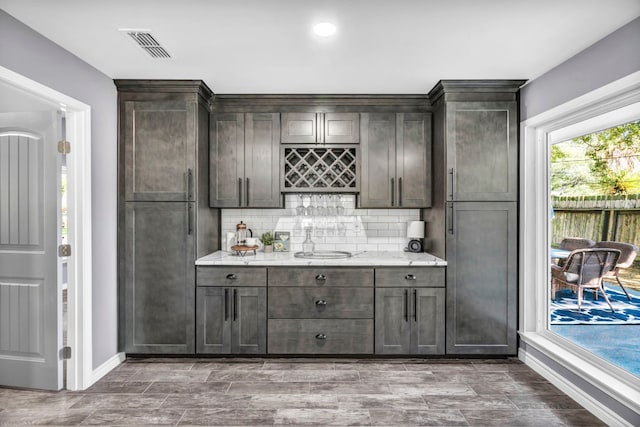 kitchen with backsplash, dark brown cabinets, and light stone counters