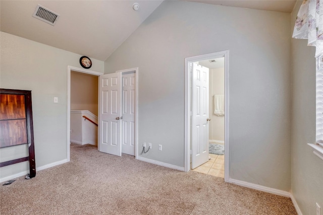 unfurnished bedroom with light colored carpet, ensuite bathroom, and lofted ceiling