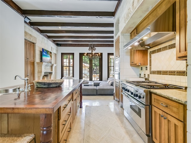 kitchen with appliances with stainless steel finishes, light tile flooring, wall chimney exhaust hood, beam ceiling, and a notable chandelier