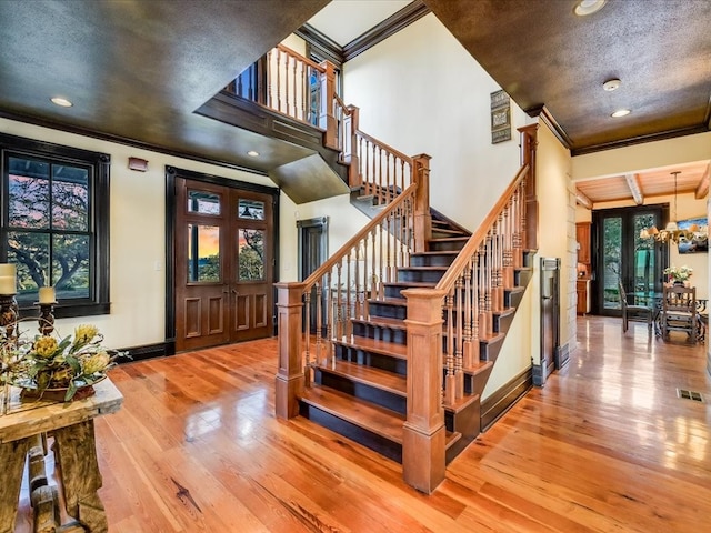 stairway with crown molding, light hardwood / wood-style floors, and a notable chandelier