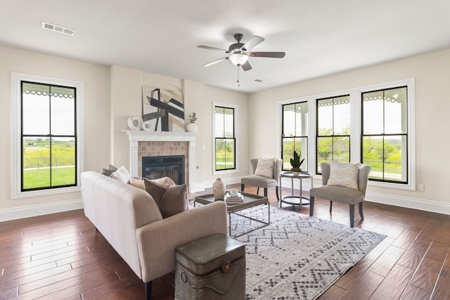 living room with ceiling fan, dark wood-type flooring, a tile fireplace, and a wealth of natural light