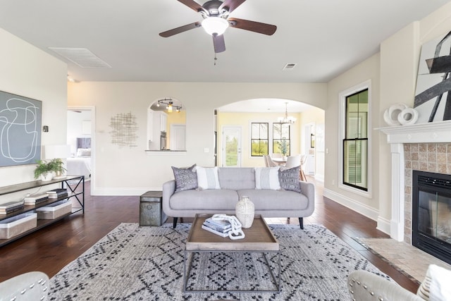 living room with dark wood-type flooring, ceiling fan with notable chandelier, and a tile fireplace