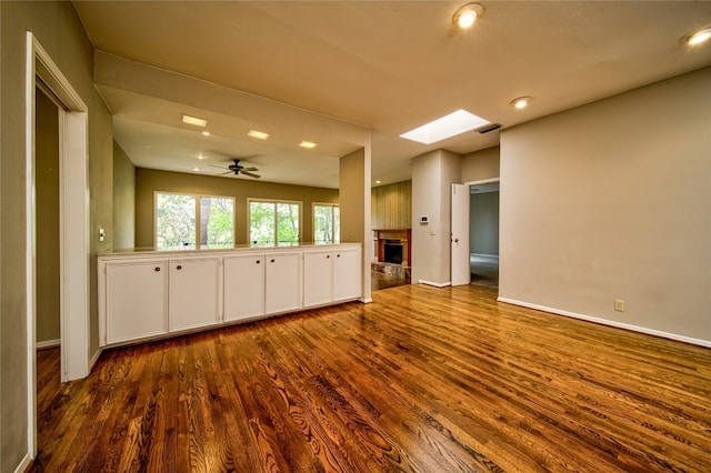 unfurnished living room featuring hardwood / wood-style flooring, ceiling fan, and a skylight