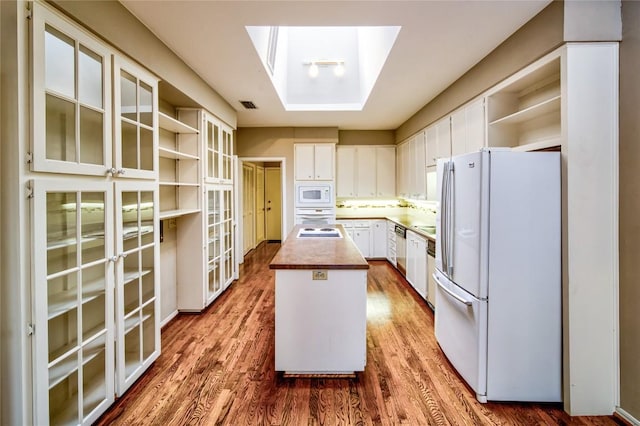 kitchen featuring white appliances, white cabinetry, hardwood / wood-style floors, a skylight, and a center island